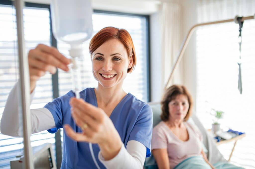 A nurse with IV drip and patient in bed in hospital room.