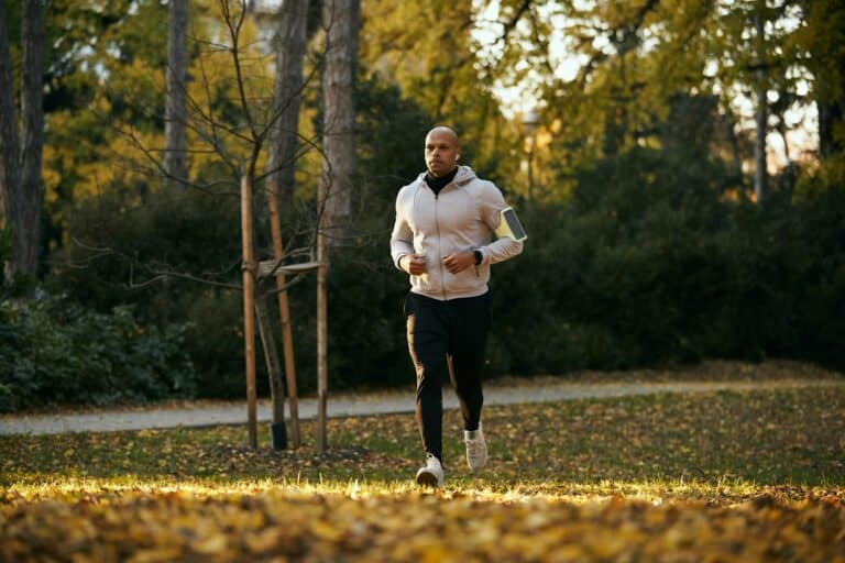 Full length of black athlete jogging in autumn park.